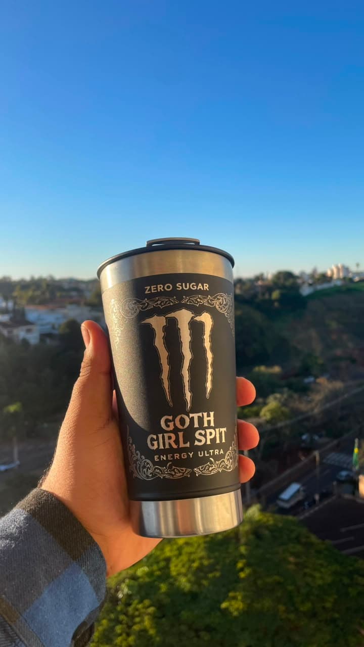 Copo térmico Goth Girl Spit segurado contra o céu azul, com a cidade ao fundo